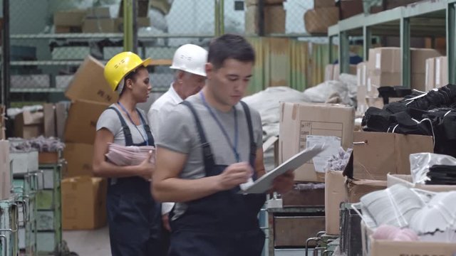 Tracking of male Asian supervisor checking good in warehouse and writing something down on clipboard