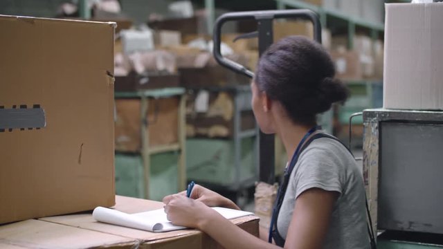 Young Latin-American warehouse worker filling paperwork on top of cardboard boxes