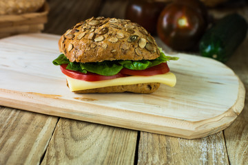 Healthy sandwich with cheese, tomatoes, lettuce on wood cutting board, rustic, selective view