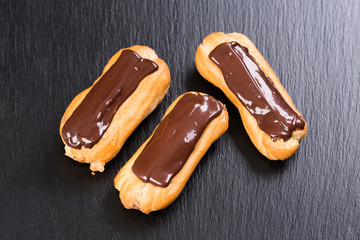 Freshly baked chocolate eclairs on black background.