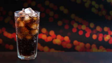 Cola with ice in glass on red bokeh background 