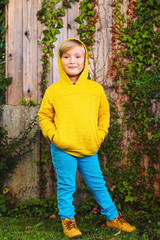 Fototapeta premium Outdoor portrait of adorable little 5 year old blond boy playing in the park, wearing yellow sweatshirt with hood, shoes and blue trousers