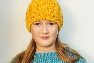 Close up portrait of cute 9 year old little girl wearing yellow hat, standing against white background