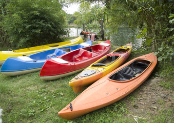 Several single and double kayaks and boats on the riverside