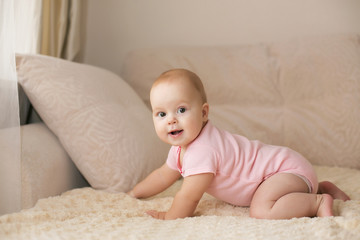 Cute smiling baby in pink bodysuit on a beige couch - 125354512