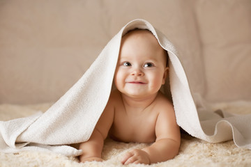 Cute smiling baby covered with white towel on a beige couch - 125354586