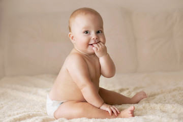 Cute smiling baby in a diaper on a beige couch - 125354590