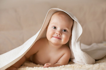 Cute smiling baby covered with white towel on a beige couch - 125354598