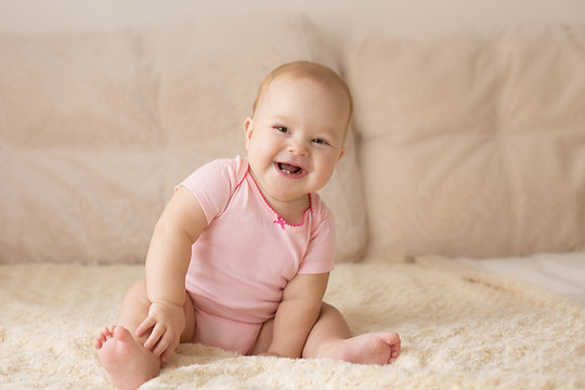 Cute smiling baby in pink bodysuit on a beige couch