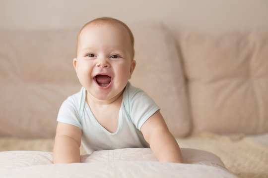Cute smiling baby in a blue body suit on a beige couch
