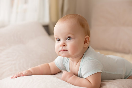 Cute smiling baby in a blue body suit on a beige couch