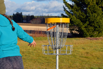 Young woman throws disc to target on disc golf course.