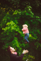 Father throws his son up in the air standing among green trees