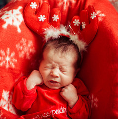 The baby in red costume lies on the carpet