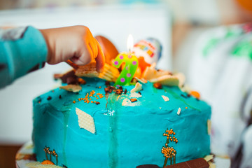 Child takes sweets from the cake with number candle two