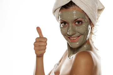 young woman with a towel on her head posing with a mask from green clay on her face