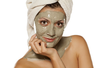 young woman with a towel on her head posing with a mask from green clay on her face