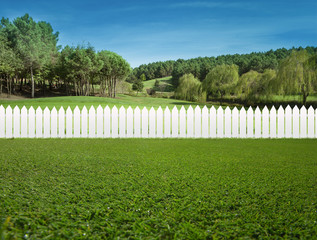 White fences on green grass and the trees behind