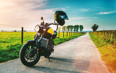 Motorrad fährt auf freier Landstrasse in den Sonnenuntergang  - obrazy, fototapety, plakaty