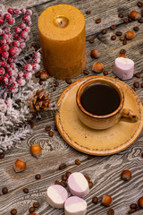 Fototapeta na wymiar Small cup of coffee, cocoa beans, hazelnuts, marshmallow, candle, fir branch in snow on wooden background