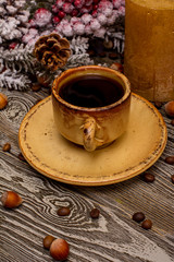 Small cup of coffee, cocoa beans, hazelnuts, candle, fir branch in snow on wooden background