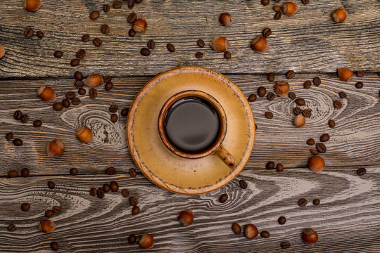 Small cup of coffee with cocoa beans and hazelnuts on wooden background