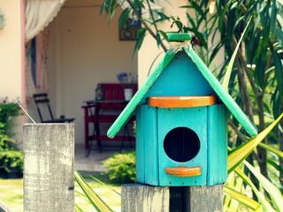 Modern bird house or nest box hangs on the wooden fence.