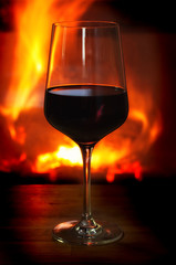 Weinglas mit Rotwein vor brennendem Kaminfeuer auf Holztisch
