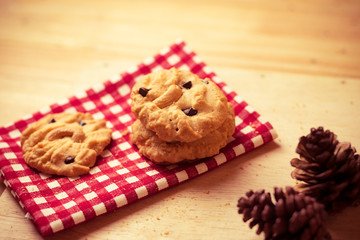 Chocolate chips and chest nut cookies on red and white checked cloth with pine cone on wood table,vintage color tone
