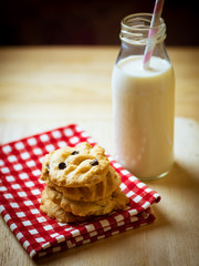 Chocolate chips and chest nut cookies on red and white checked cloth with milk and paper party straws on wood table, low key light
