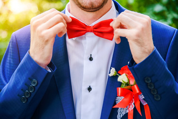 The groom in a blue suit corrects a red butterfly