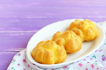 Tasty stuffed profiteroles. Homemade fresh profiteroles with with cream filling on a plate and on lilac wooden background. Closeup
