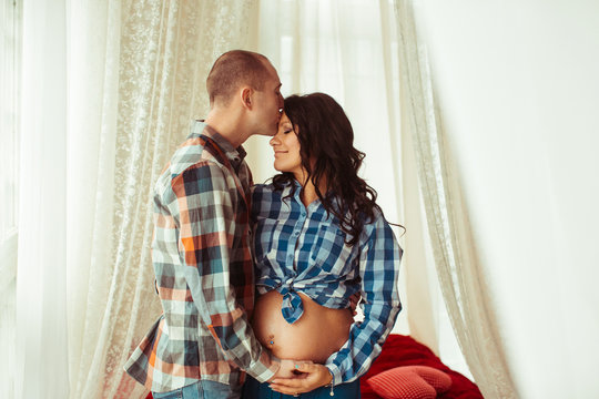 Tall Man Kisses Head Of His Pregnant Woman While Hugging Her Bel