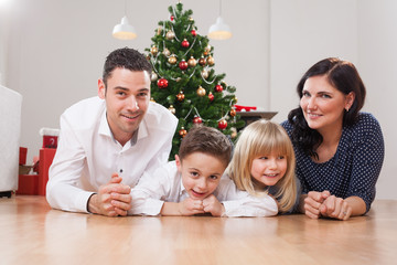 family lies in front of christmas tree