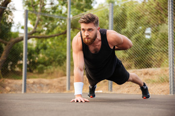 Attractive bearded sportsman doing push-ups with one hand outdoors