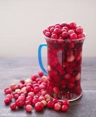 Fresh juicy cranberry in a glass transparent mug on a wooden surface of a table, close up