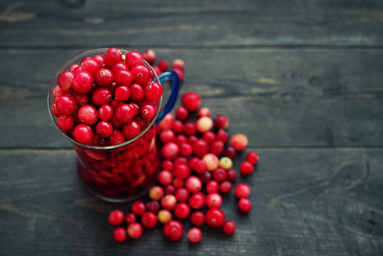 Fresh juicy cranberry in a glass transparent mug on a wooden surface of a table, close up