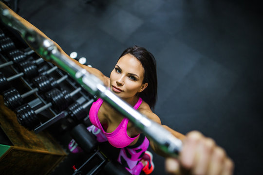 close-up, portrait of a girl in the gym. Girl doing exercise on the back muscles in a block simulator. Profel, girl's head rolled a little to us. Girl dressed in a pink top