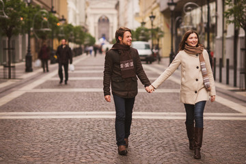 Christmas in old town. Young cheerful caucasian couple in warm cozy clothes walking in city centre.