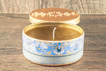 Handmade candle made in the golden rounded box decorated with textured fabric. Scenery and wooden background.