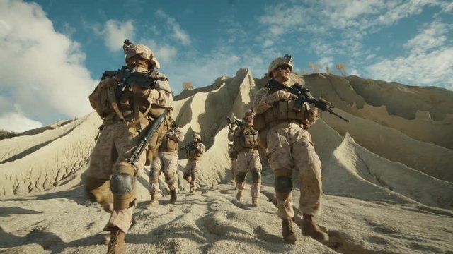 Squad of Fully Equipped and Armed Soldiers Walking down the Hill in the Desert. Slow Motion.
