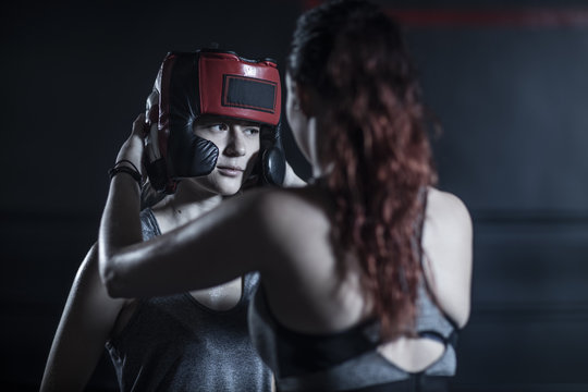 Woman helping female boxer putting on head guard