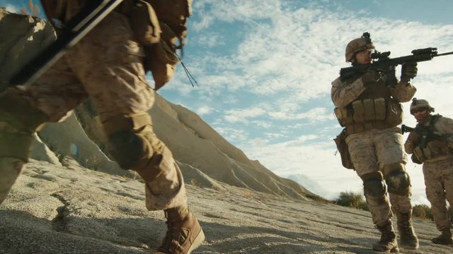 Squad of Fully Equipped and Armed Soldiers Walking in Single File in the Desert. Slow Motion.