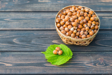 Hazelnuts in a straw basket with a green leaf of a hazel grove on a wooden background. Copy space for text