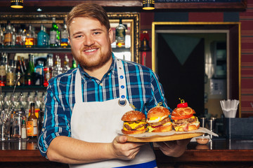 Chef in apron presenting a tray with different delicious burgers