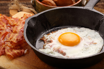 Fried egg with hot bacon pieces in a cast iron skillet