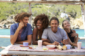 Four friends at a table by the sea looking to camera, Ibiza