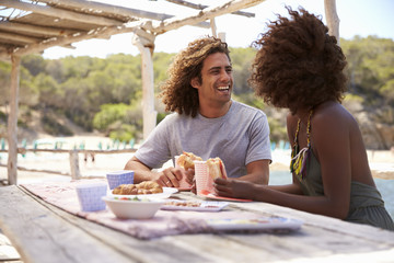 Young couple eating at a table by the sea look at each other