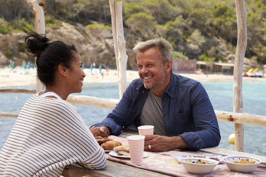 Middle Aged Couple Smiling Across A Table By The Sea, Ibiza