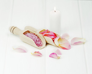Still life with beautiful rose petals and spatula with sea salt on white painted wooden background.